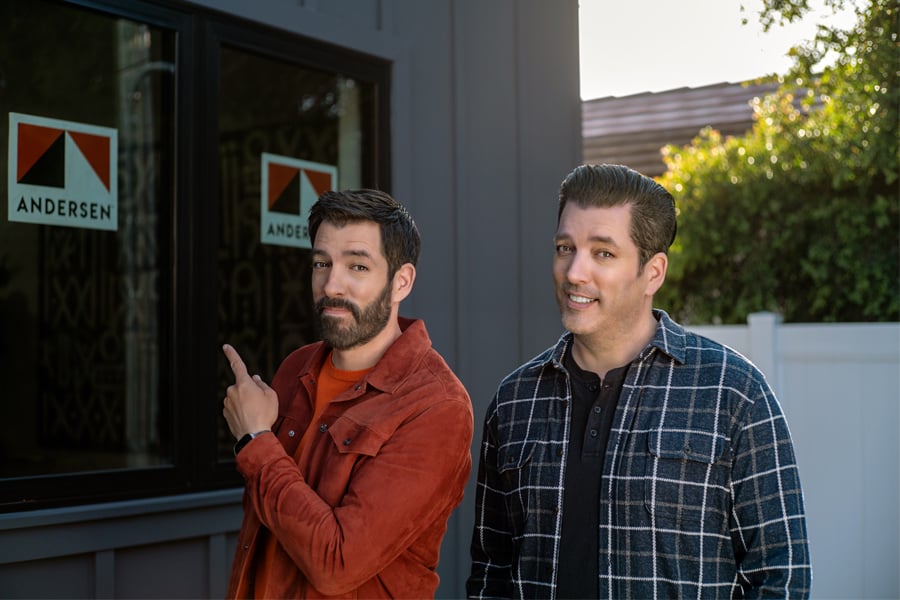 Drew and Jonathan Scott standing in front of new home with Andersen Windows stickers on the windows
