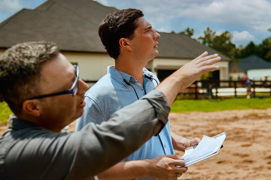 Two men stand on a building site discussing a project.