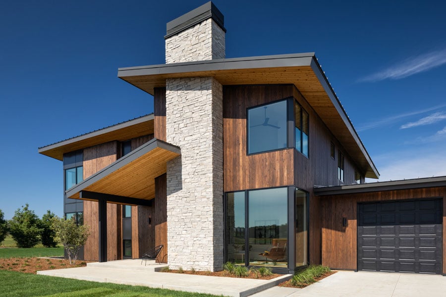 A modernist cedar-clad home with oversized eaves and black floor-to-ceiling windows stands out against the blue skies of a summer’s day.