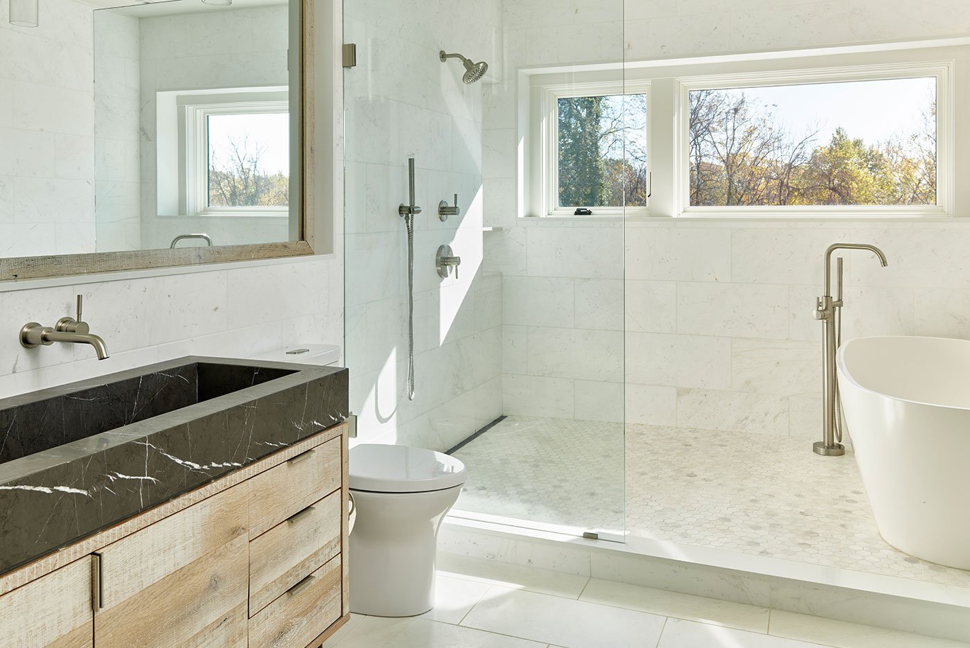 A bathroom with wet room combining shower and tub mixes black stone, white tile, and natural wood cabinetry.