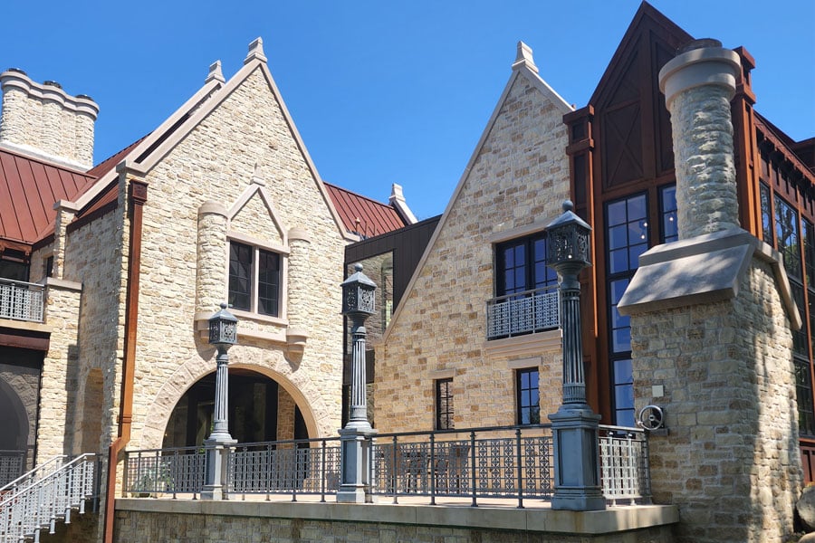a stone building with gothic architectural features, including pointed arches, decorative columns and steeply pitched roofs. The building has multiple levels, large windows and a mix of stone and wood elements