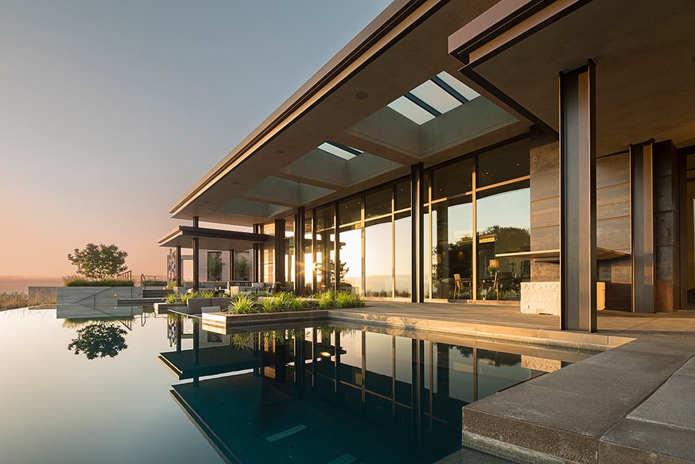 Infinity pool at sunset with modern house with large windows and doors