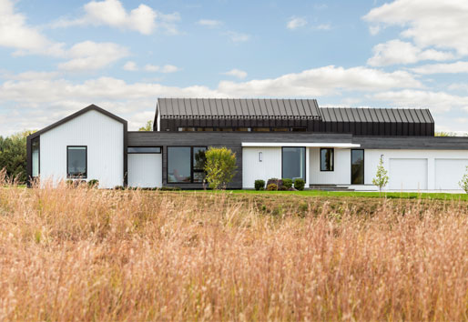 A contemporary prairie home with a unique look featuring a combination of siding types including black standing-seam metal, white polyash, and a thermally treated wood.