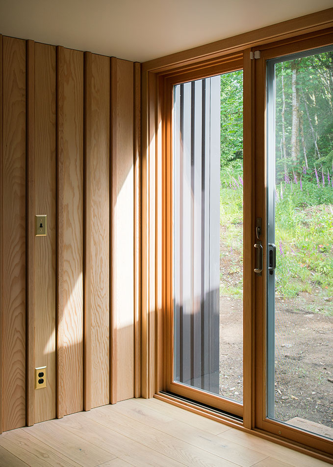 An interior shot of an entryway with wood paneling and wood floors facing an E-Series Gliding Patio Door with sidelight.