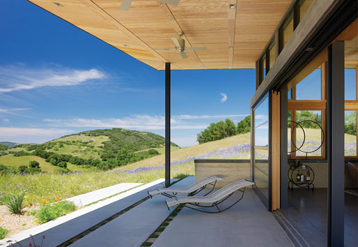 A roof overhang shading a patio with rolling tree-covered hills in the background.