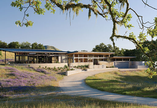 A view down a curved driveway of the home, which is characterized by a long, low-slung profile.