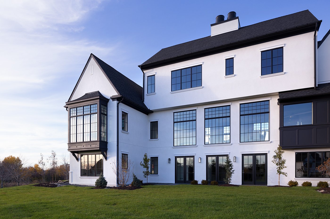 A modern Tudor home with black windows, doors, and roof set against a white exterior and green lawn.