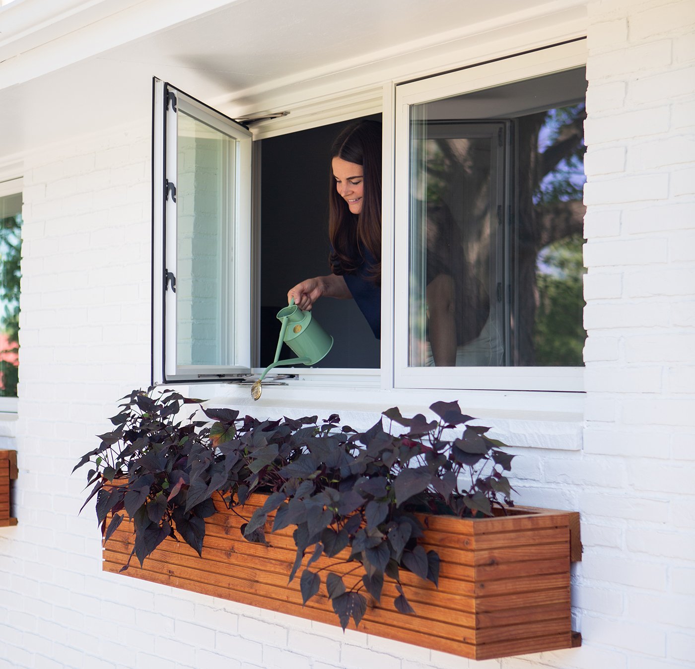 A woman waters the plants in her window box through an open 100 Series Casement Window.