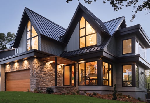A two-story modern home with large 400 Series windows lit up at dusk. 