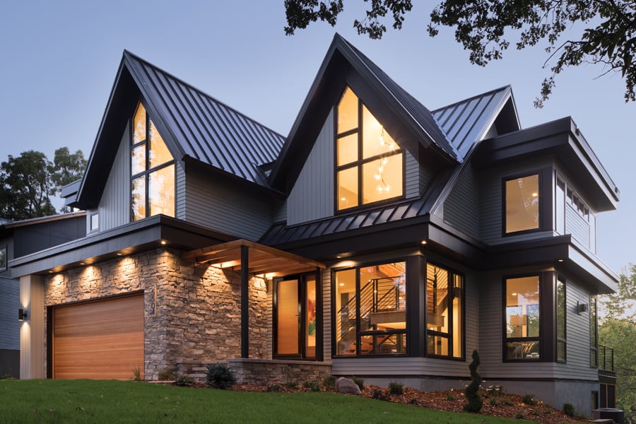 A two-story modern home with large 400 Series windows lit up at dusk. 