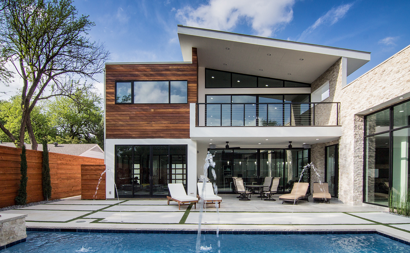 An exterior view of a white and wood modern home with lots of windows and doors facing the swimming pool.