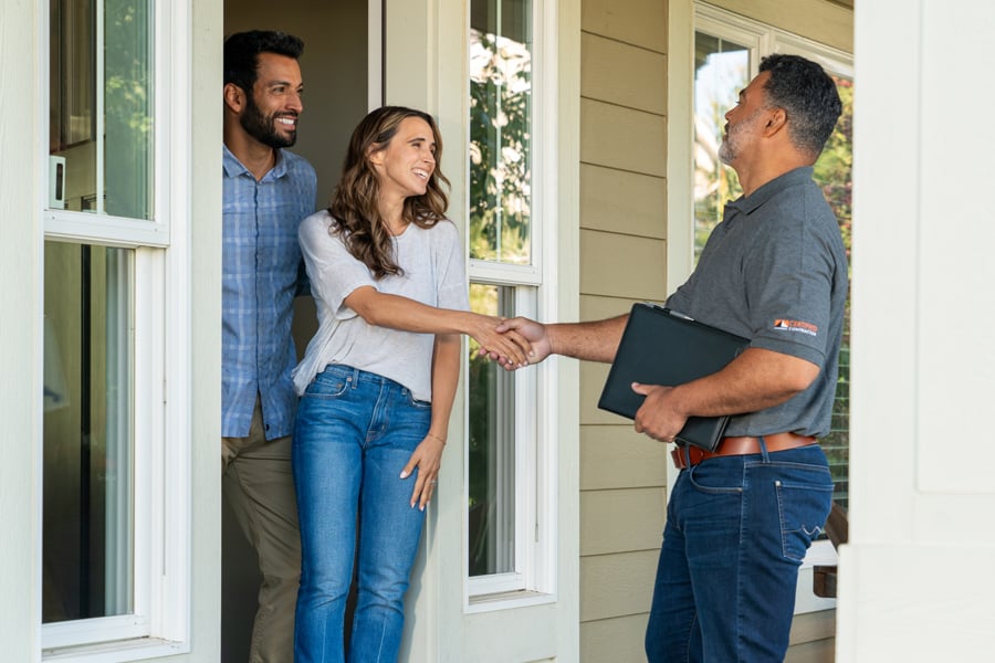 A man and woman stand in their front door greeting a contractor who is standing on their porch.