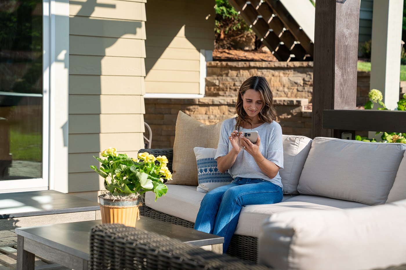 A woman sits on an outdoor sofa reading her phone.