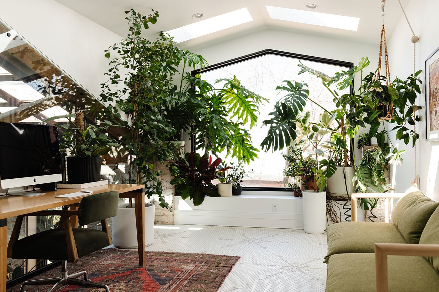 A lofted home office space with a large-scale picture window with a plant-filled bench underneath that’s furnished with desk and loveseat.