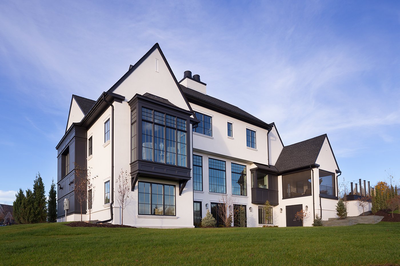An exterior shot of a new construction Tudor home with white exterior and black windows, roof, and other features.