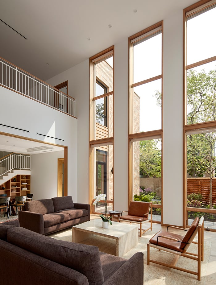 double-height living room with floor-to-ceiling windows that have natural wood frames. 