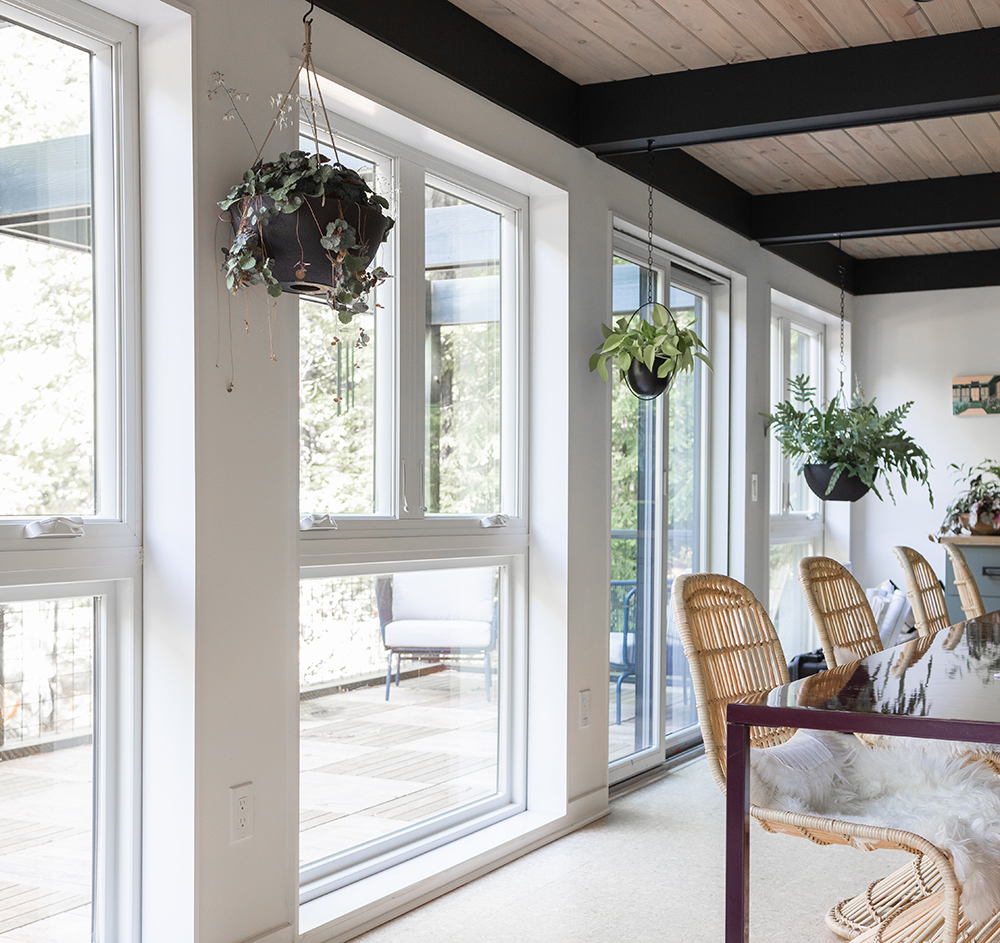 A wall with casement and picture windows and a gliding patio door with white interiors, wicker chairs and hanging plants.  