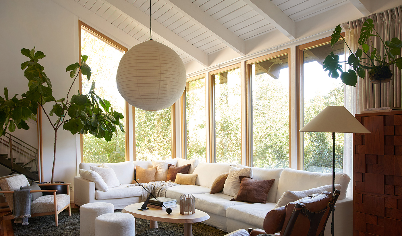 A living room with a large white couch and chairs, dark gray rug and a wall of picture windows with white oak frames.