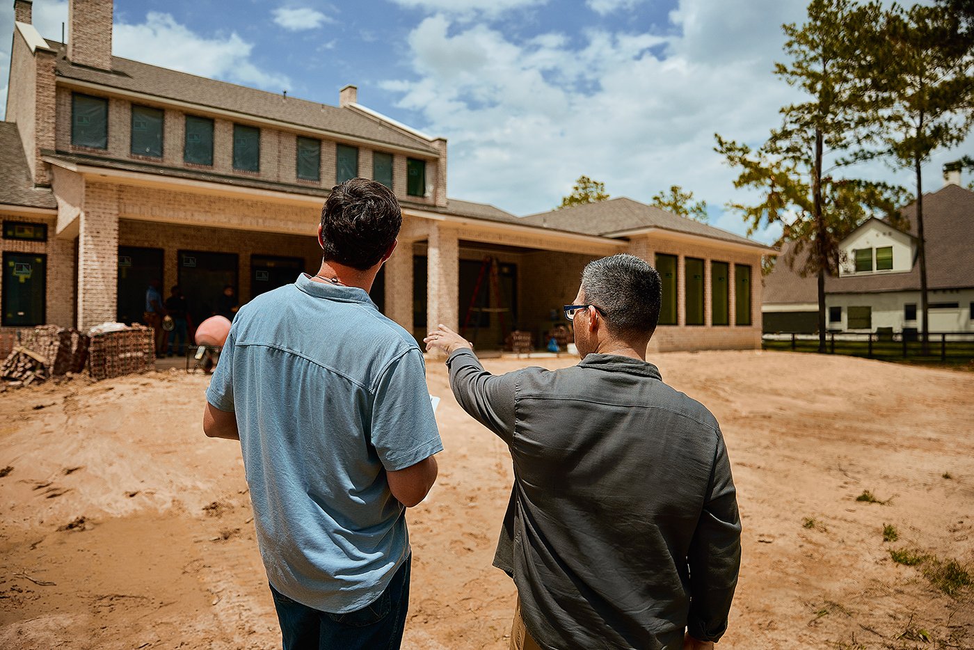 Two men stand on a job site discussing an under-construction home