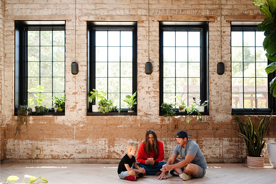A family plays a card game under a bank of windows in a home with industrial design. 