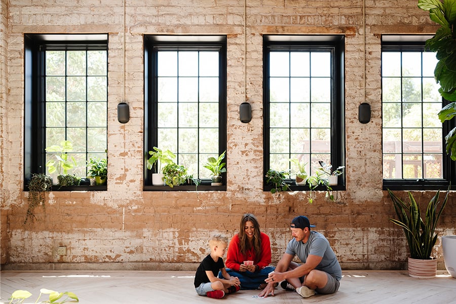A family plays a card game under a bank of windows in a home with industrial design.