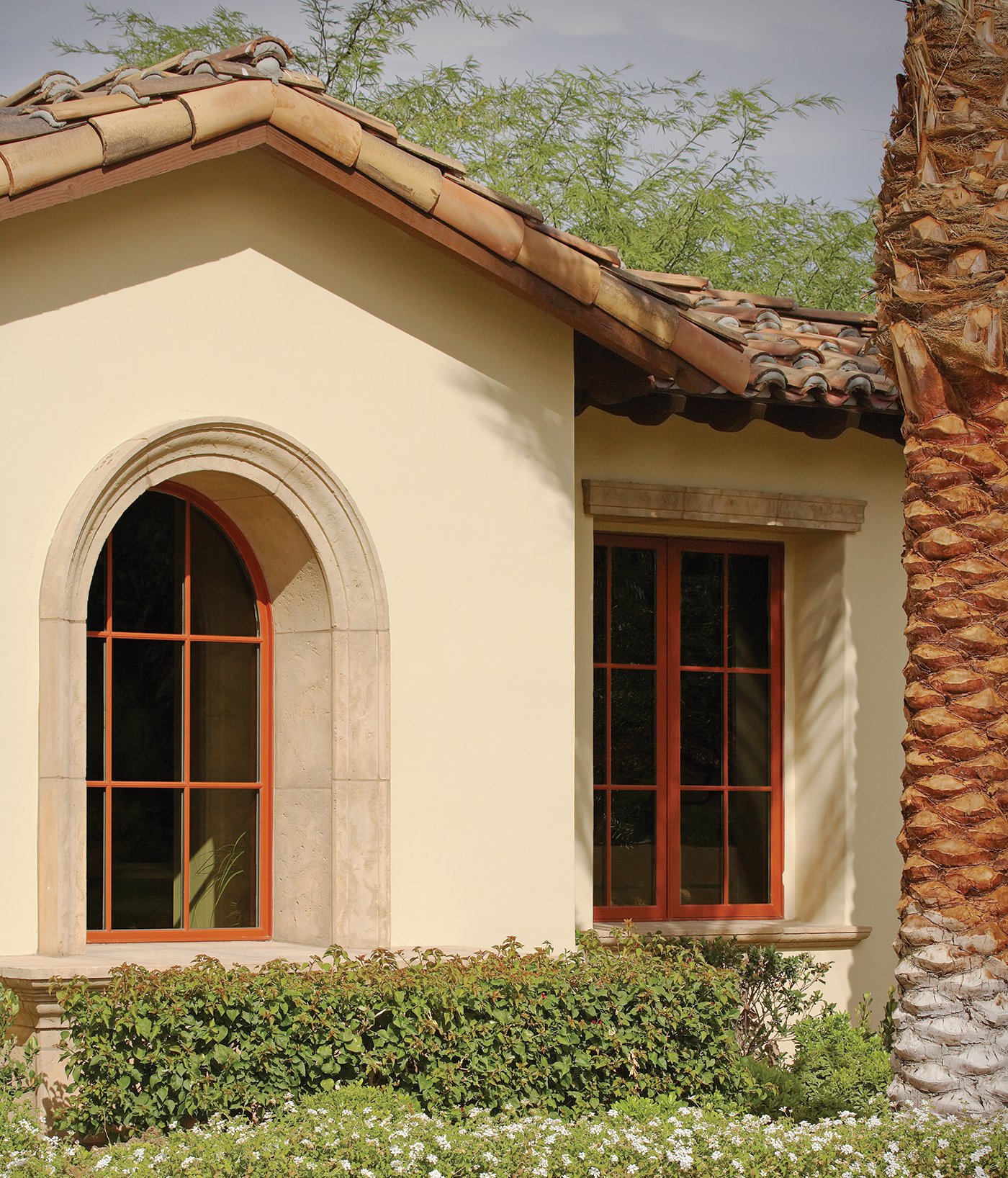A Spanish-style stucco home with a tile roof and an arched specialty window with a burnt orange exterior and colonial grilles. 