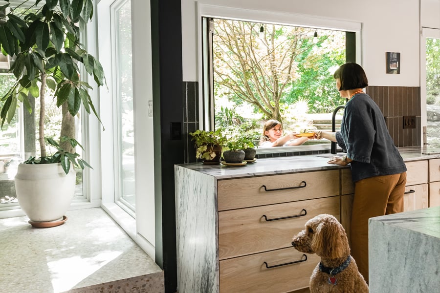 A woman hands a plate of food out her Folding Pass-Through Window to a child outside.