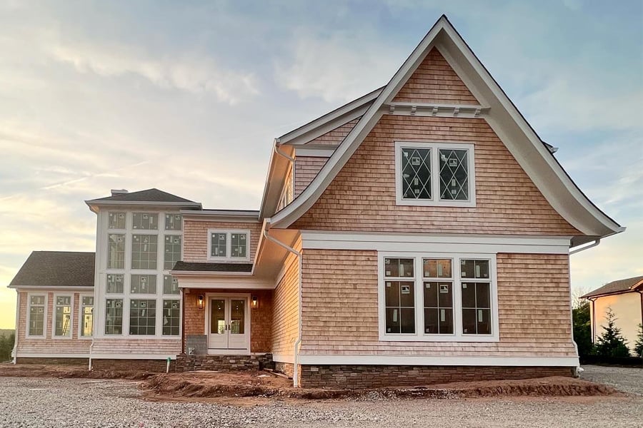 An under-construction home with a cedar shake siding and white Andersen® 400 Series windows.