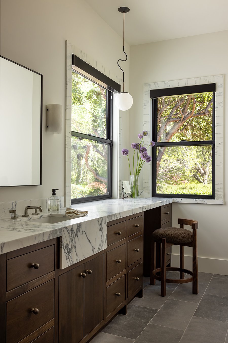 A bathroom with dark walnut cabinetry and marble counters and trim around the Andersen 100 Series Single-Hung Windows.