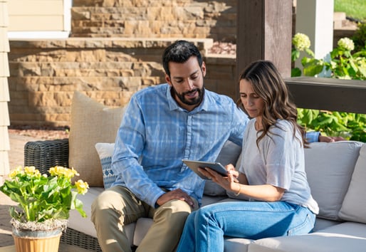 A couple seated on a patio look at a tablet together.