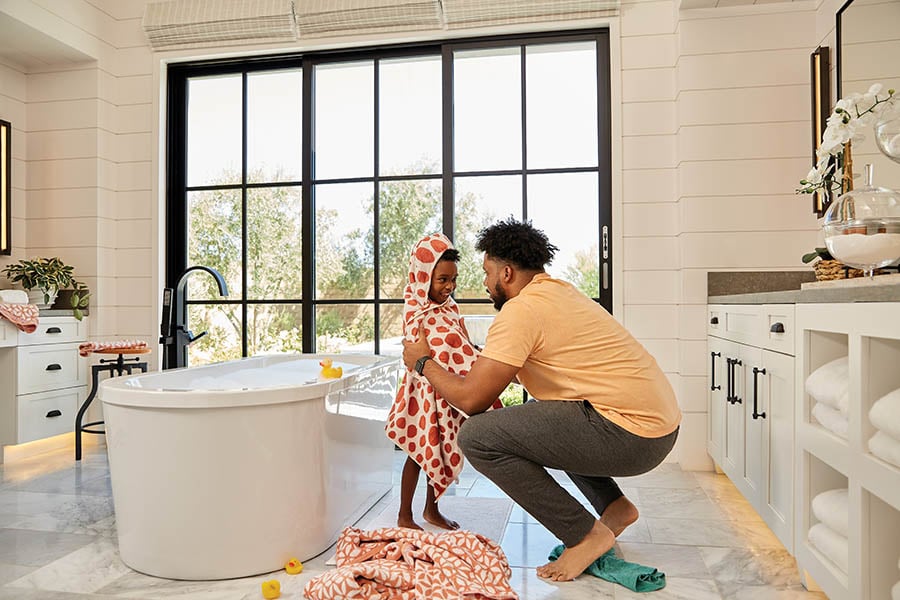 Adult and kid inside white bathroom with a dark bronze Andersen Heritage Multi-Slide Patio Door with full divided grilles