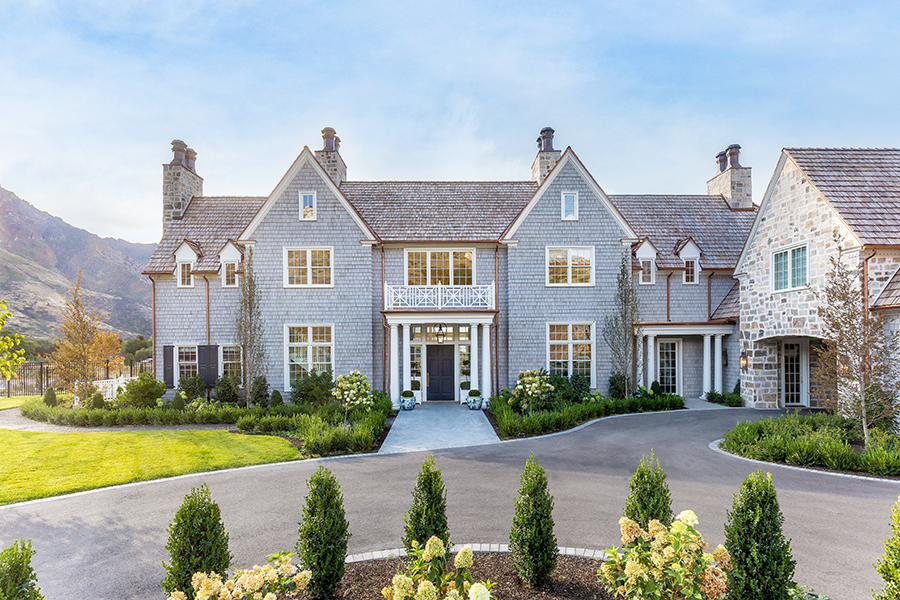 A blue two story home with white windows, brick chimneys, and hills in the background.