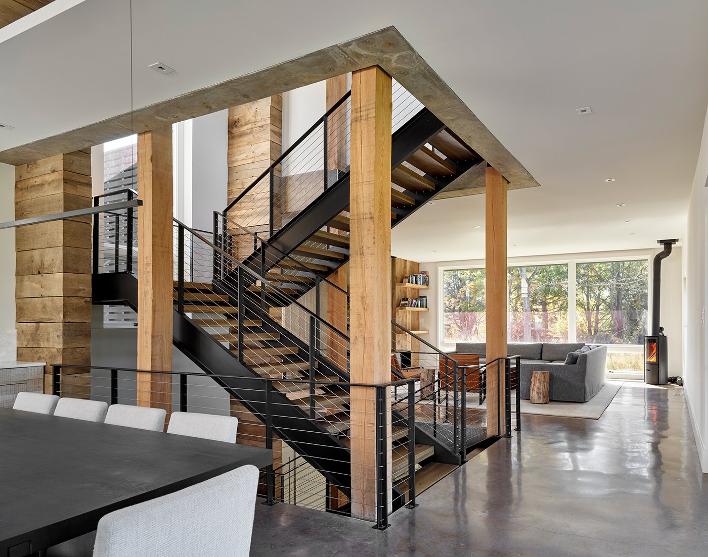 An indoor living area with a central staircase, exposed wooden ceiling beams and black dining table. 