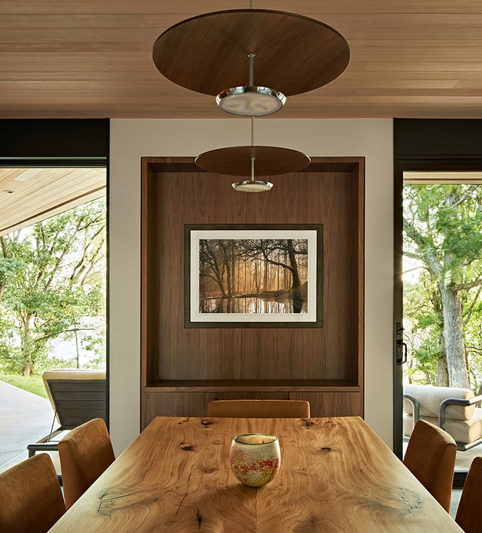 A dining room with floor-to-ceiling glass and a hallway beyond that ends in an Andersen® E-Series Picture Window.