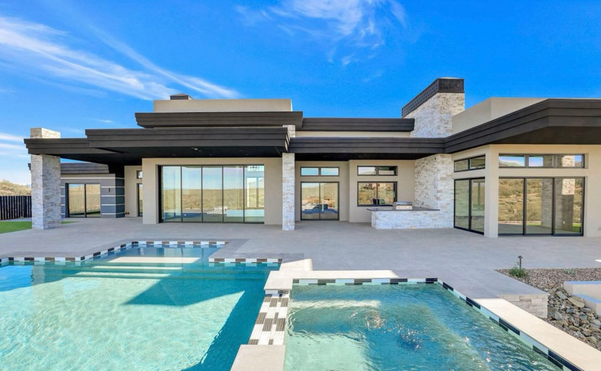 The outside of a contemporary luxury home in the desert rendered with a pool and large expanses of glass created by black Andersen® Aluminum Multi-Slide Doors and 100 Series Gliding and Picture Windows.