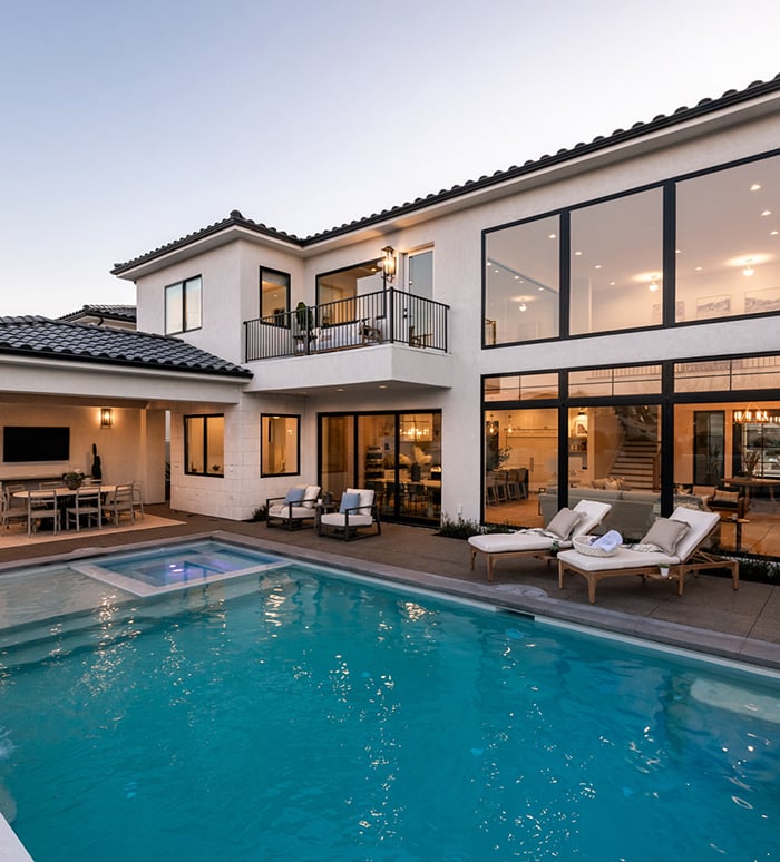 An outdoor dining area next to an underground pool with large, black windows and doors allowing deck access