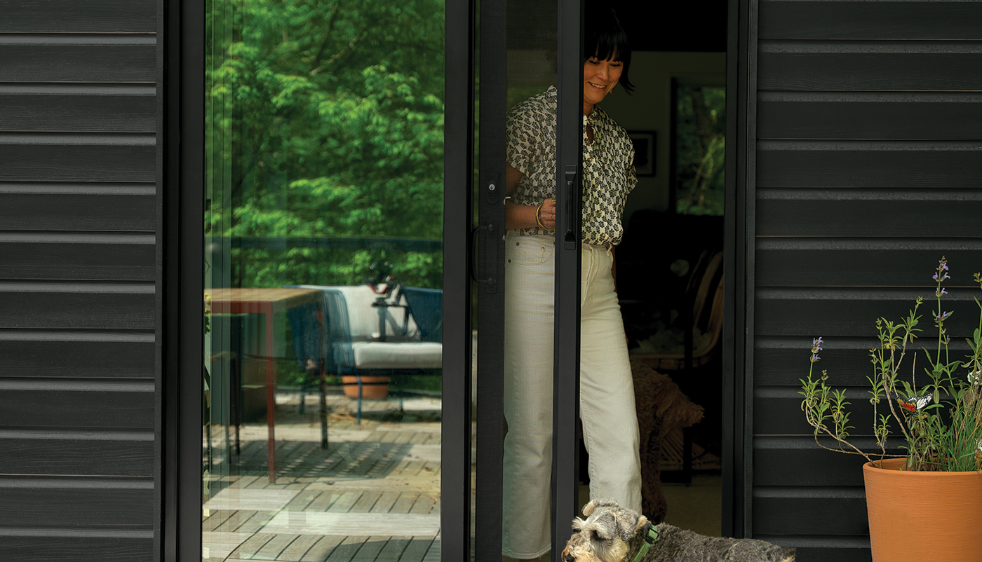 A woman pulls a retractable insect screen across the opening side of her Andersen 200 Series Narroline Gliding Patio Door.