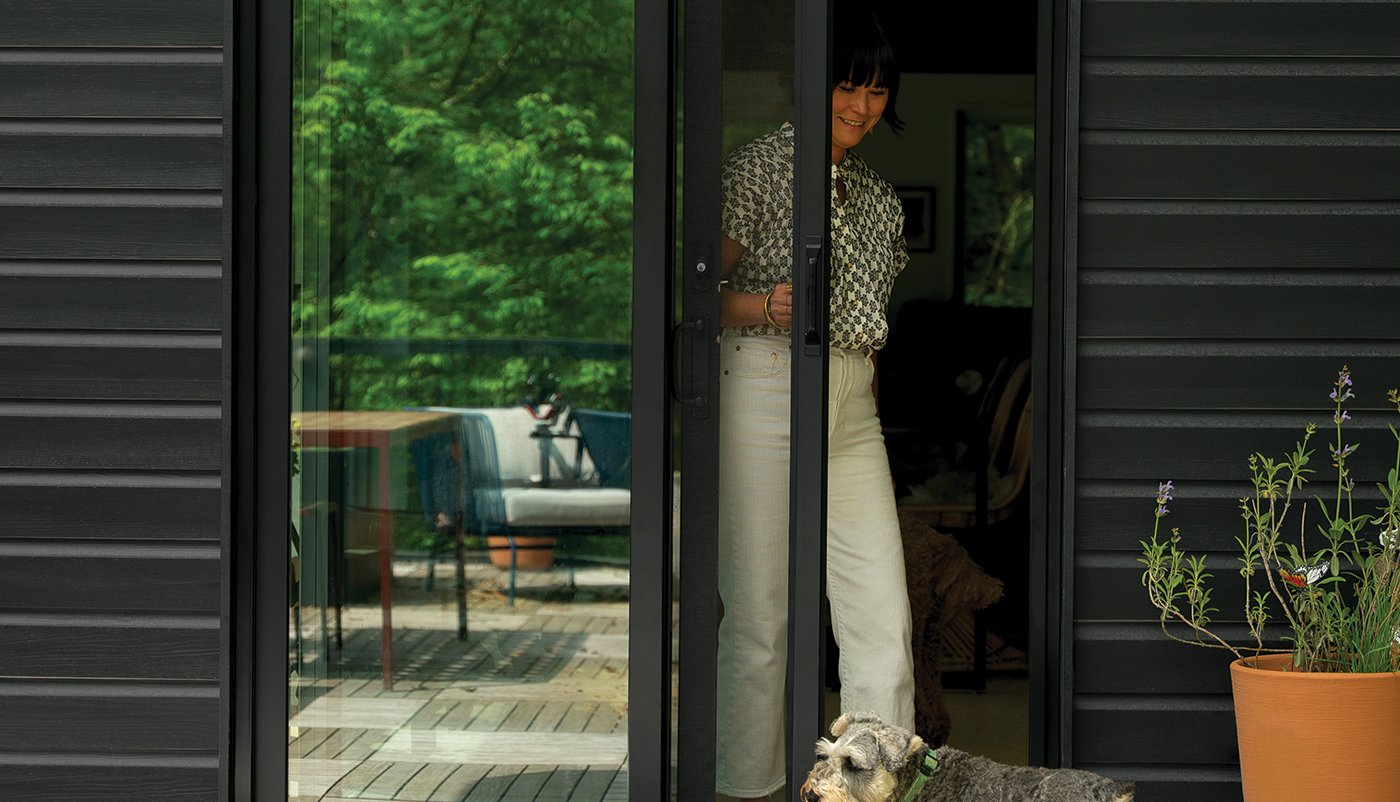 A woman pulls a retractable insect screen across the opening side of her Andersen 200 Series Narroline Gliding Patio Door.