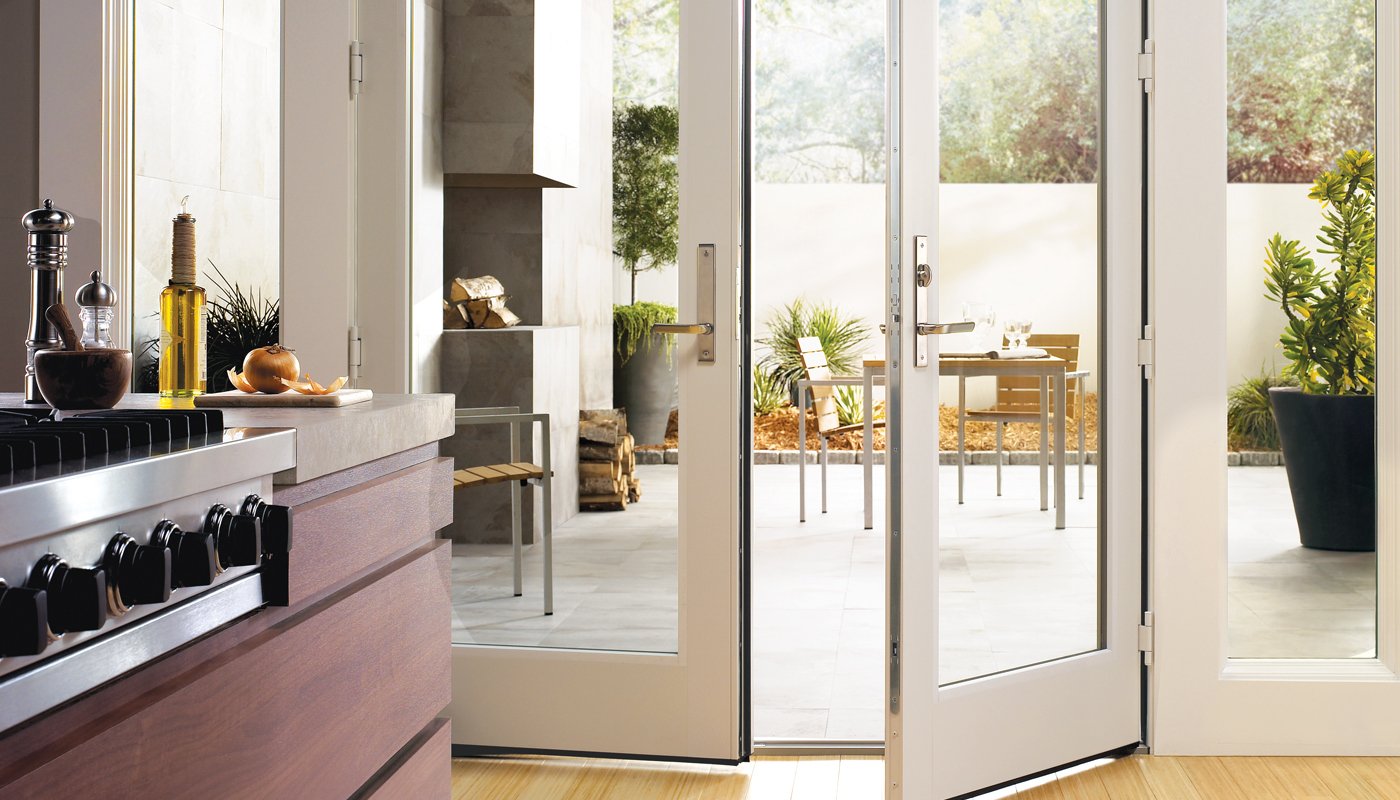 A sleek, modern kitchen with white Andersen 200 Series Hinged Patio Doors leading to a patio