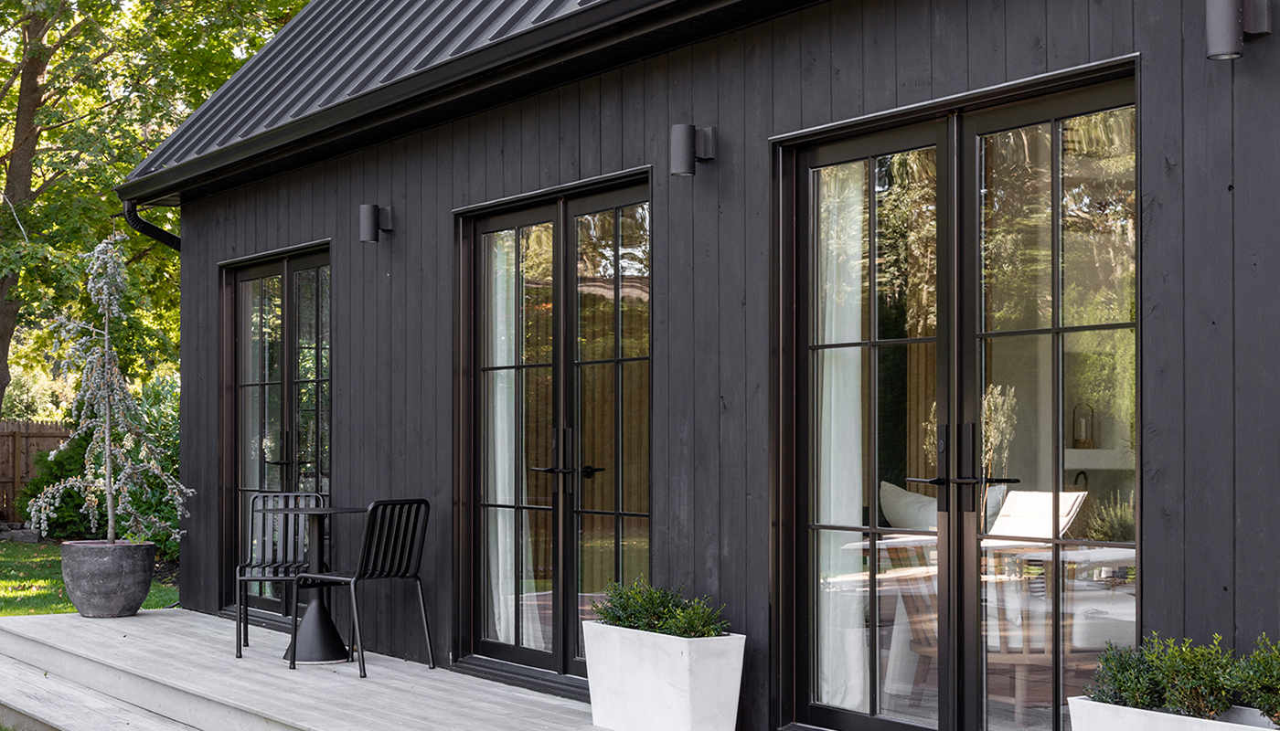 A single-story black home with metal roof and three sets of Andersen® E-Series Hinged Patio Doors.