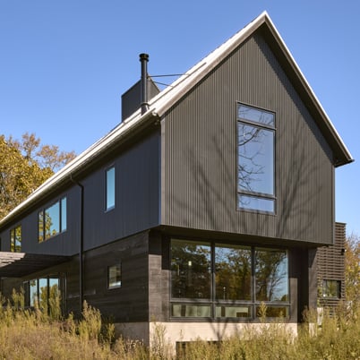 A black barn home in a field with A-Series windows and doors with contemporary profiles.
