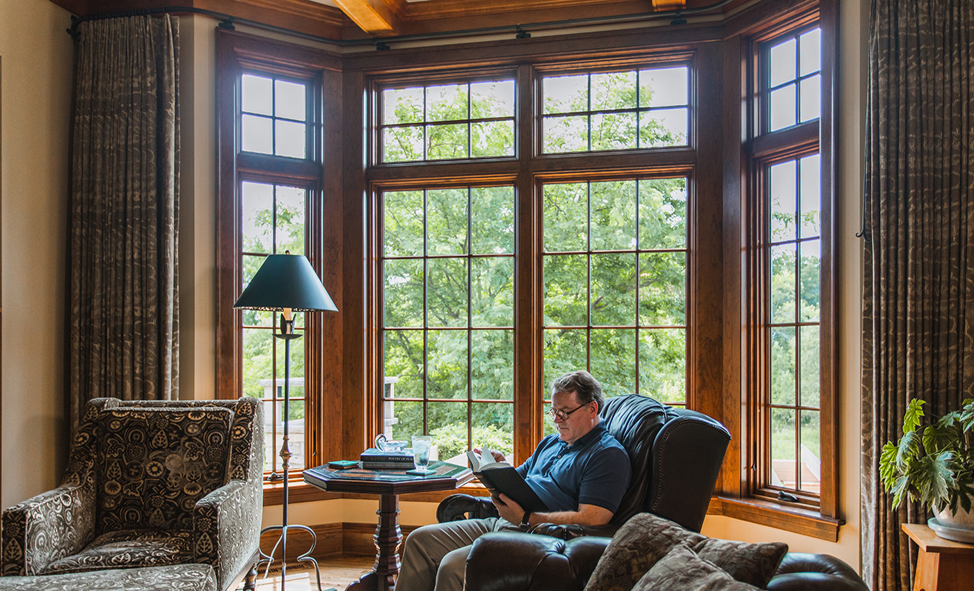 A bay window brings light into a living room where a man reads in an easy chair.