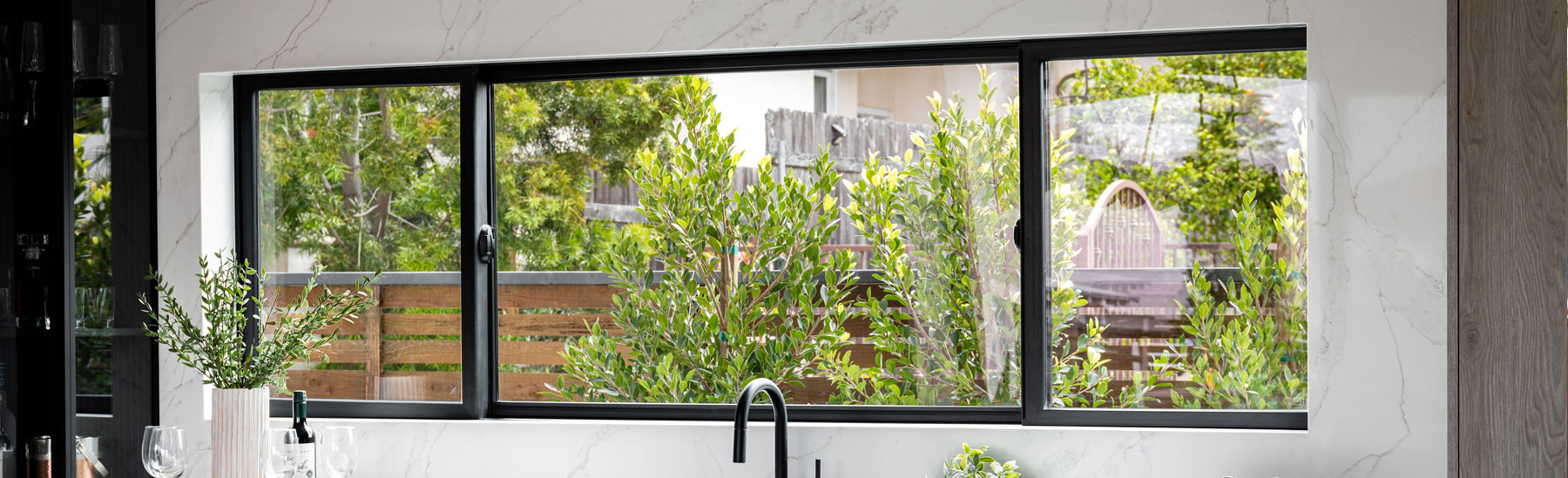 A kitchen with an extra-wide Andersen® 100 Series Gliding Window installed into a marble backsplash above the sink.