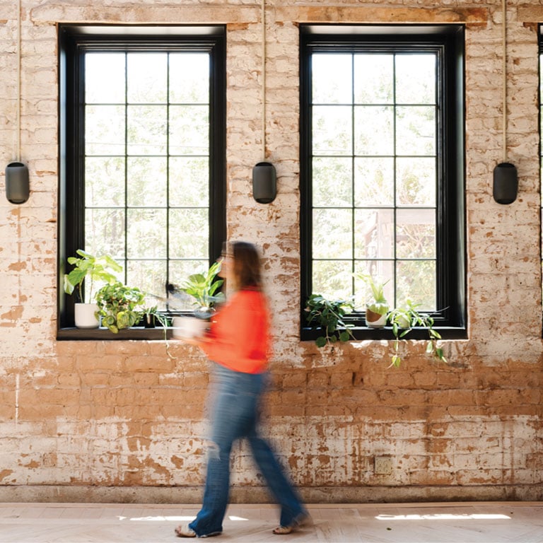 women walking in front of black framed windows in brick interior