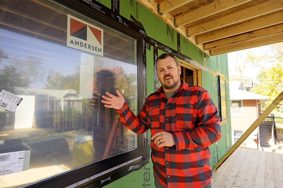 A man stands next to an Andersen® window that’s been installed in an under-construction home.
