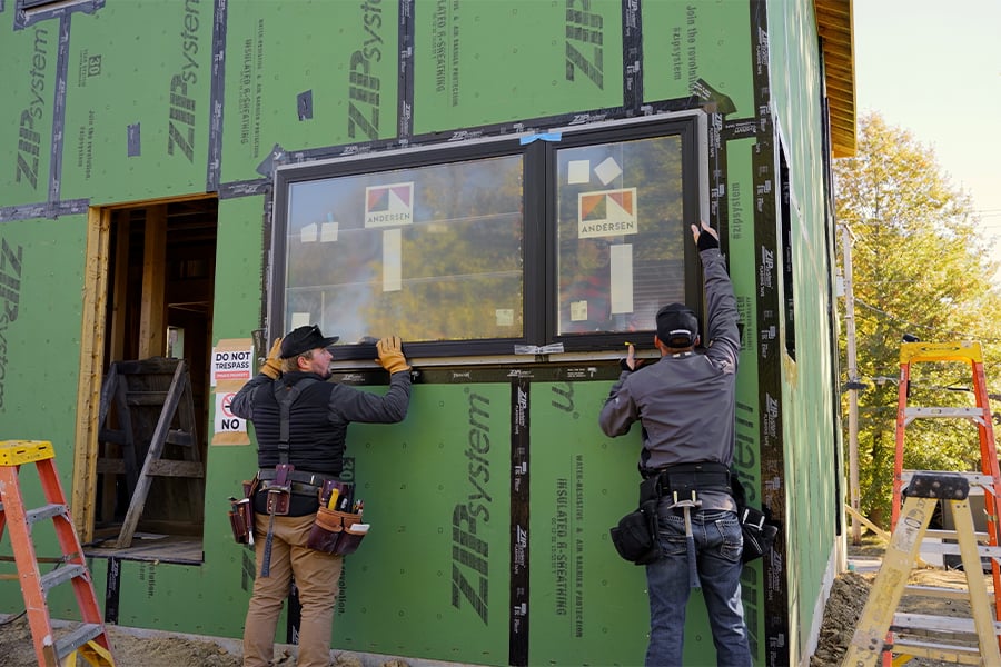 Two men install a window in an under-construction home.