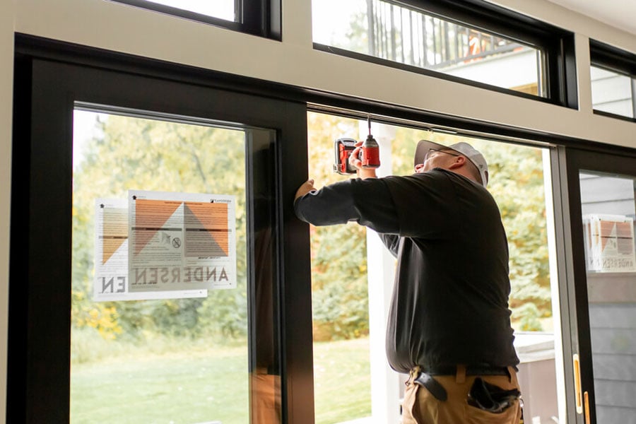 A contractor installs a new patio door with black frames and black-framed transom windows above