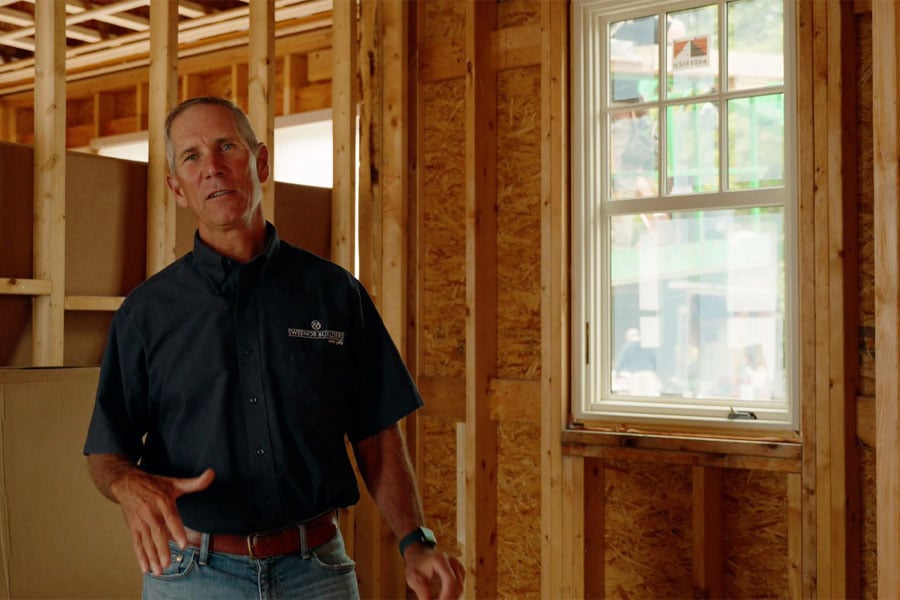 Builder Jeff Sweenor stands next to a window in a framed-out new construction home.