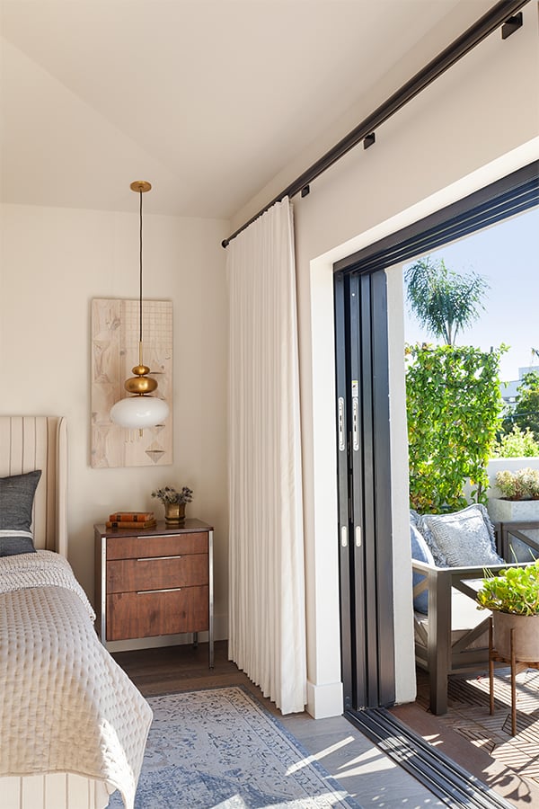 A bedroom with an open MultiGlide Door that pockets into the wall and connects with a balcony outside.