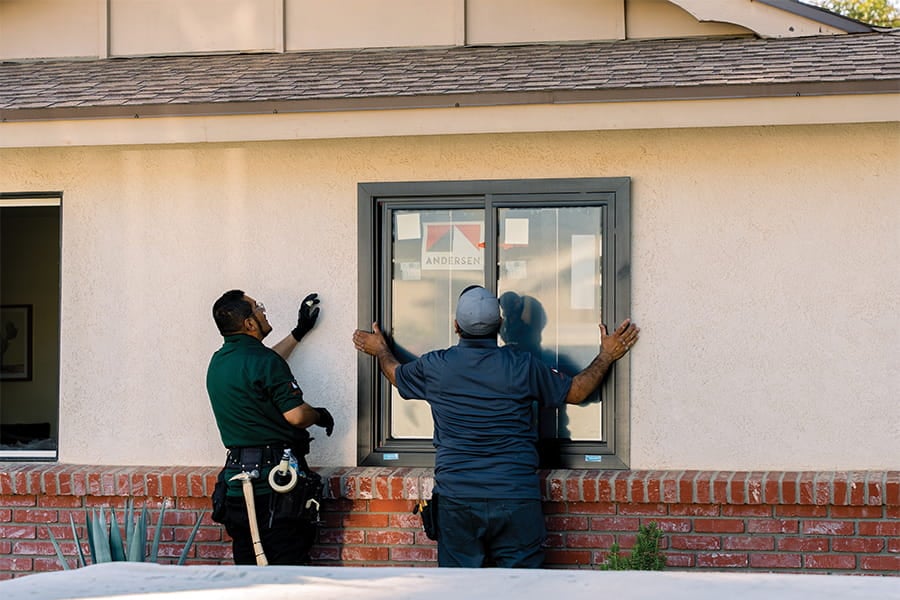 Two contractors install a window in a stucco home.
